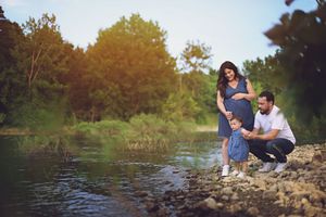 A couple in casual attire shares an intimate moment by a tranquil lake at sunset among trees.