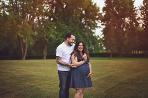 A couple shares a tender moment together on a grassy field during sunset with trees in the background.