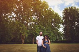 A couple stands together on grass in a park during golden hour with trees in the background.