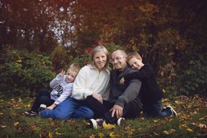 A family lies together on autumn leaves during an outdoor photo session in a wooded setting.
