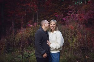 A romantic couple embraces in front of vibrant red autumn foliage during an outdoor photo session.