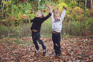 Two children play in a pile of autumn leaves on a crisp fall day in the woods.