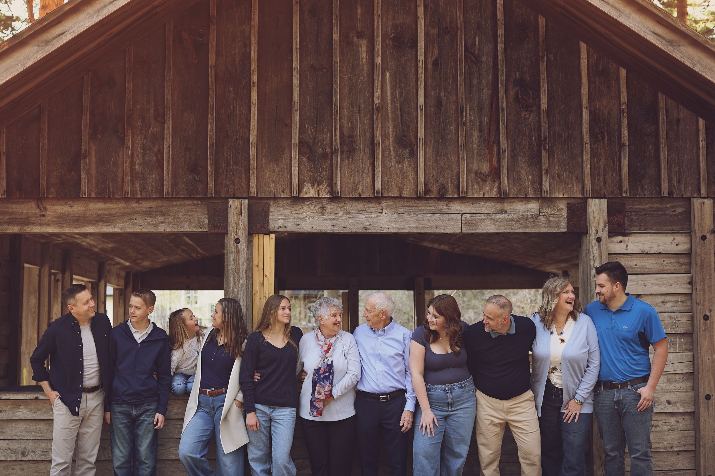 A large multigenerational family poses together outdoors under a rustic wooden covered bridge structure.