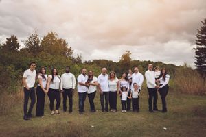 A large family group wearing coordinated white outfits poses together outdoors.