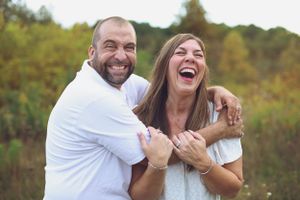 A happy couple laughing together outdoors in casual white attire.