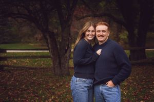A couple embraces outdoors during an autumn photo session with fallen leaves on the ground.