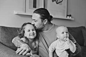Black and white candid photograph of a parent sitting on a couch sharing an affectionate moment with two young children.