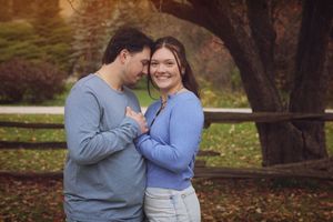 A couple shares an intimate moment together in a park during autumn with fallen leaves on the ground.