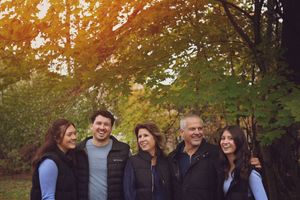 A group of people stand together outdoors at sunset with autumn trees in the background.
