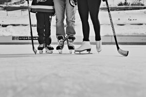 Close-up of three people in ice skates holding hockey sticks on an outdoor rink in winter.