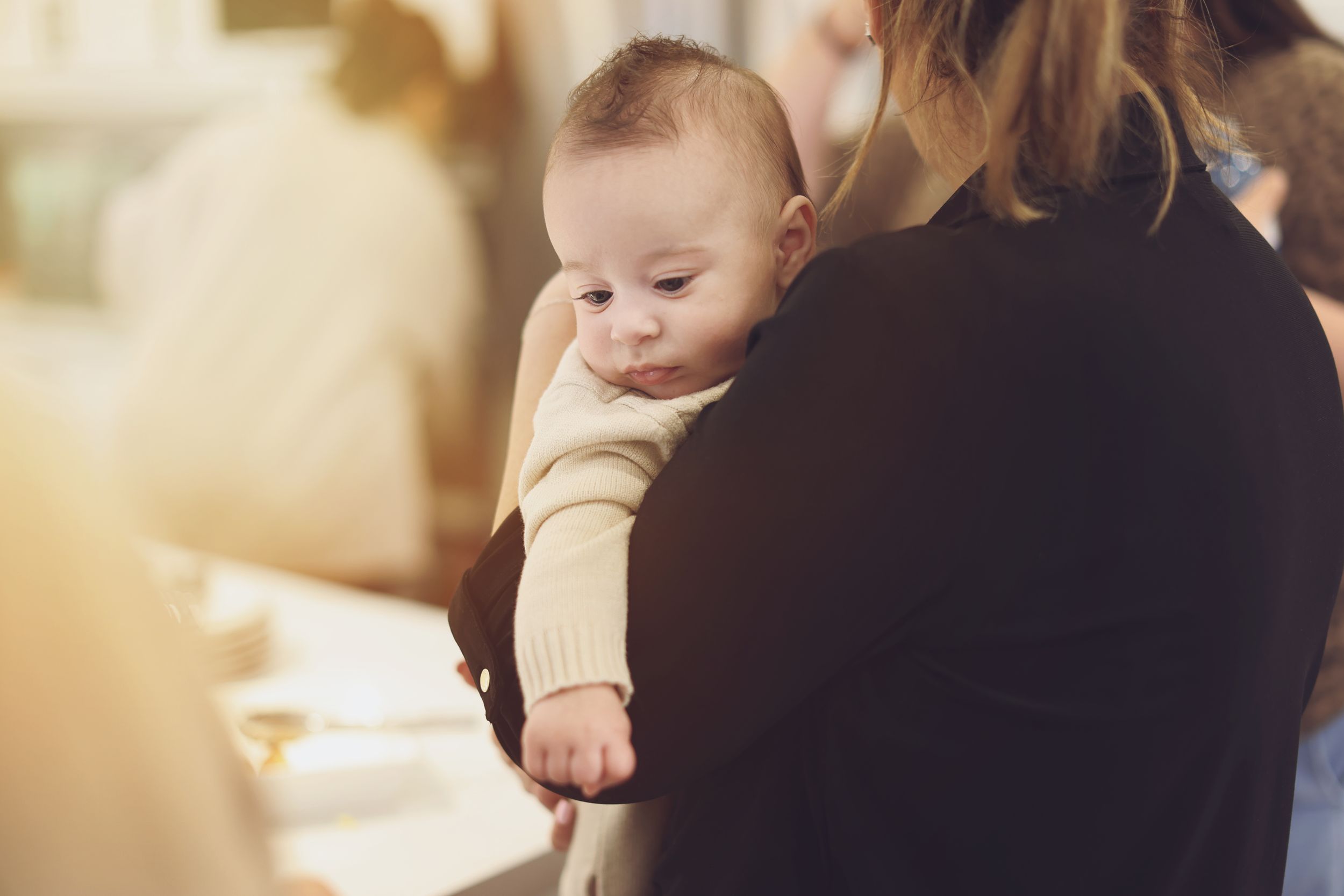 A mother gently holds her newborn baby on her shoulder in a warmly lit indoor setting.