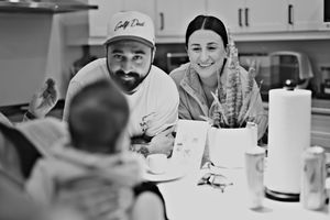 Black and white photo of a smiling couple sitting together at a kitchen table with their baby.