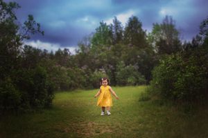 Person in yellow raincoat stands on rural path surrounded by moody nature landscape.