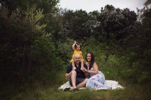 A family sits together on a white blanket for an outdoor portrait session in a natural wooded setting.