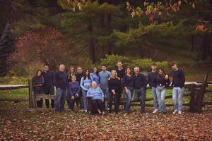 A large group stands together on fallen autumn leaves in a park setting during fall season.