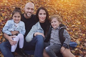 Family group sitting together on fallen autumn leaves in a park during golden hour.