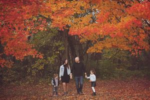 A family stands together under vibrant red and orange autumn maple trees in a forest setting.