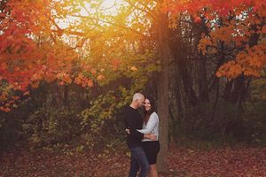 Couple embraces under vibrant autumn foliage during golden hour in a forest setting.