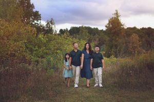 A family portrait taken in a field with autumn foliage in the background.