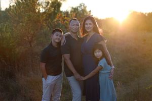A family portrait silhouetted against a warm sunset with trees in the background.