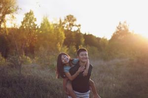 A romantic couple enjoying a playful piggyback ride at sunset in a natural outdoor setting.