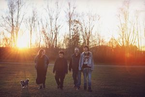 A group silhouetted against a golden sunset in an open field with their dog.