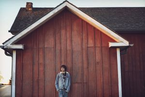 A rustic red wooden barn wall with white trim serves as backdrop for a casual portrait.