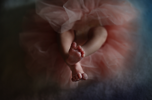 Tiny baby feet peek out from pink tulle fabric in a dreamy portrait setting.