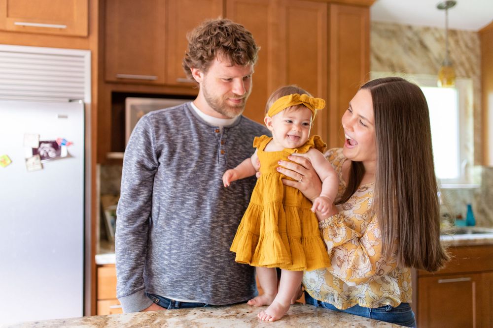 A happy family moment captured in a kitchen with a smiling baby in a bright yellow dress.