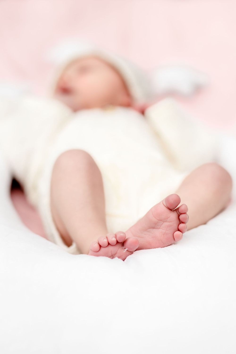 Close up of tiny baby feet against white blanket with pink background.