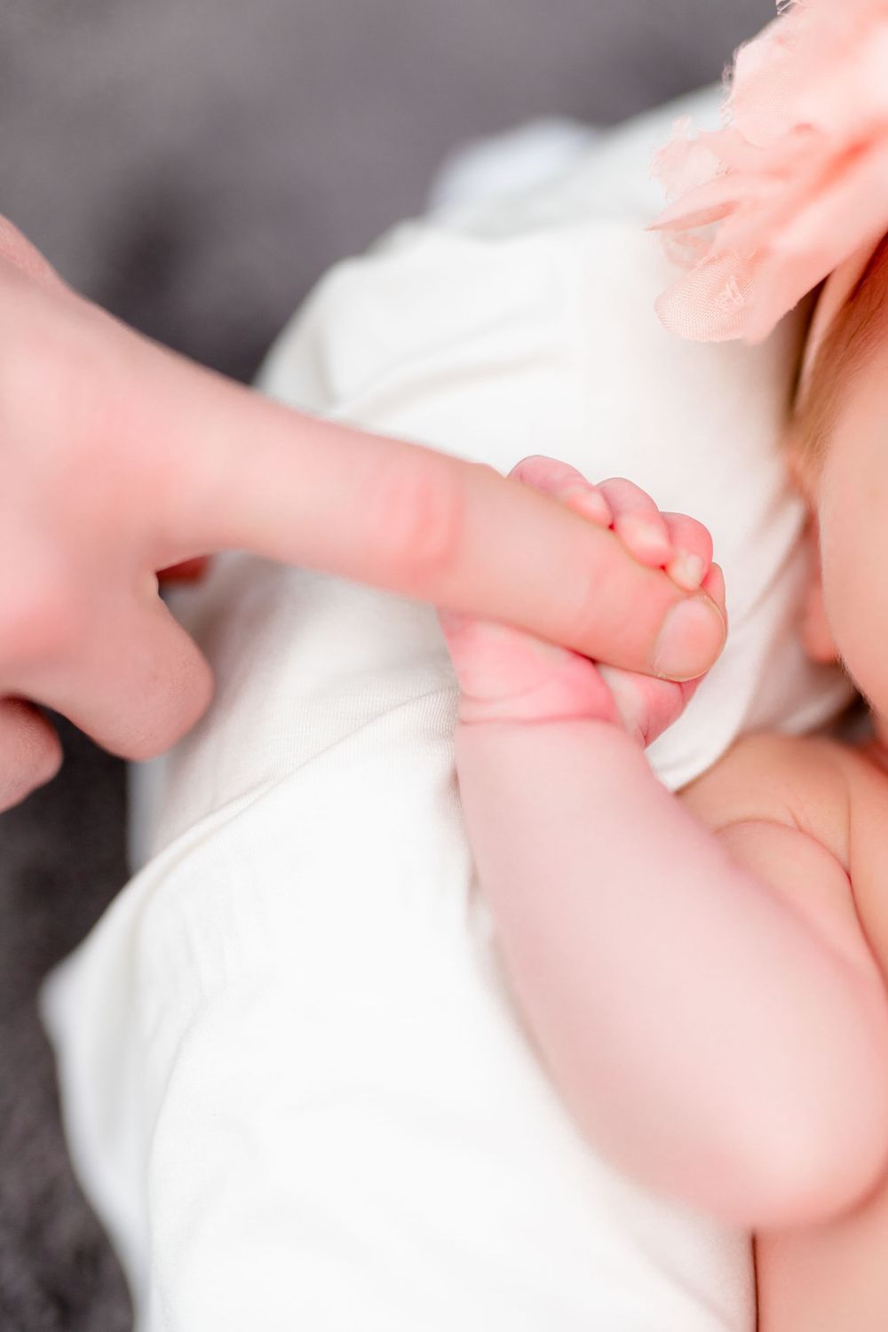 Close up of baby's tiny hand being held against white fabric.