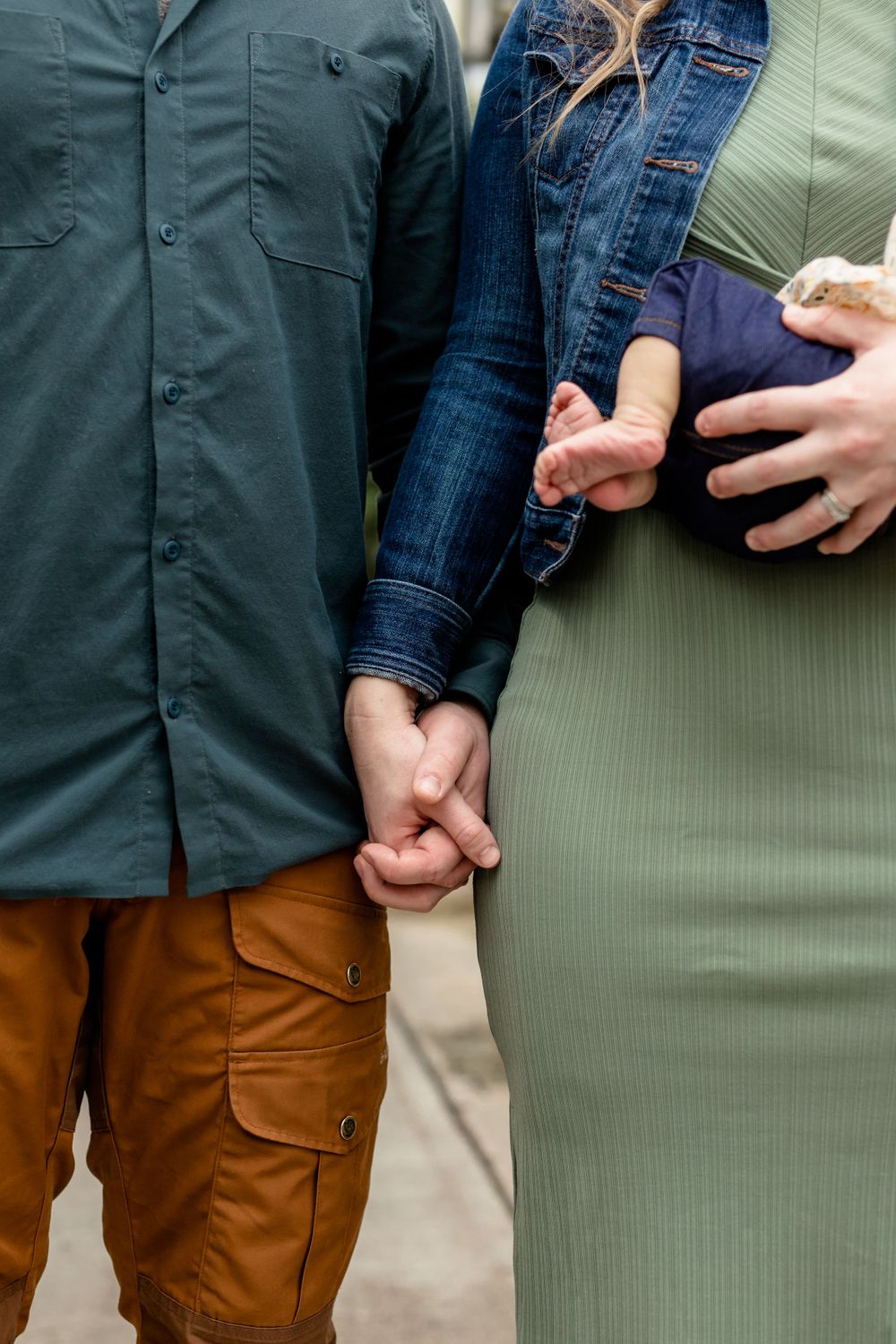 A close-up of hands holding together while wearing casual clothing against a green background.