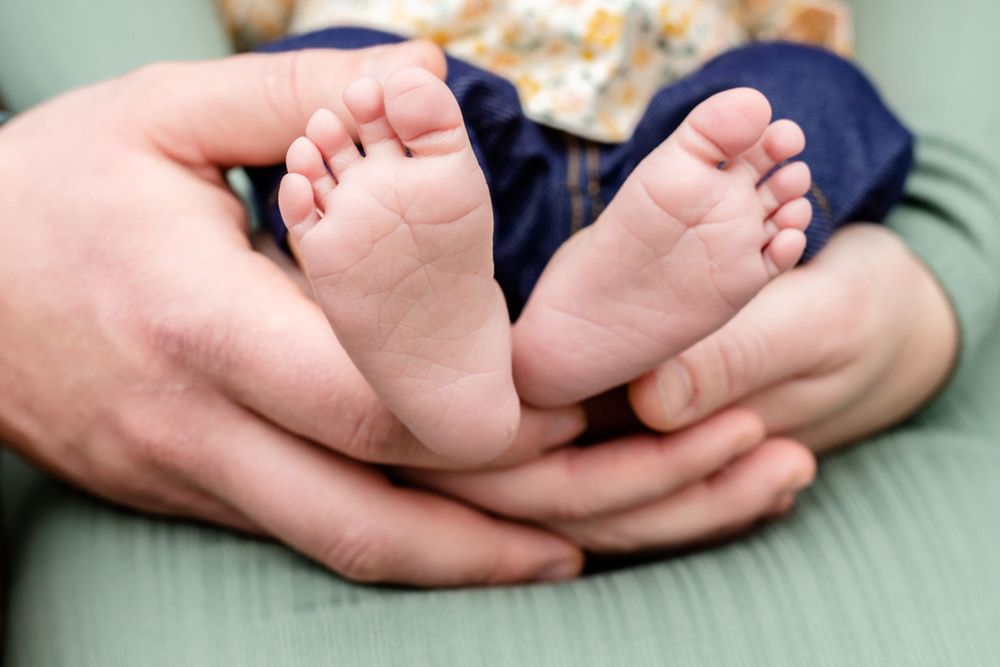 Tiny baby feet resting in gentle hands against a soft green surface.