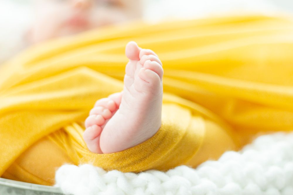 A tiny baby foot peeks out from yellow fabric against a white knitted blanket.