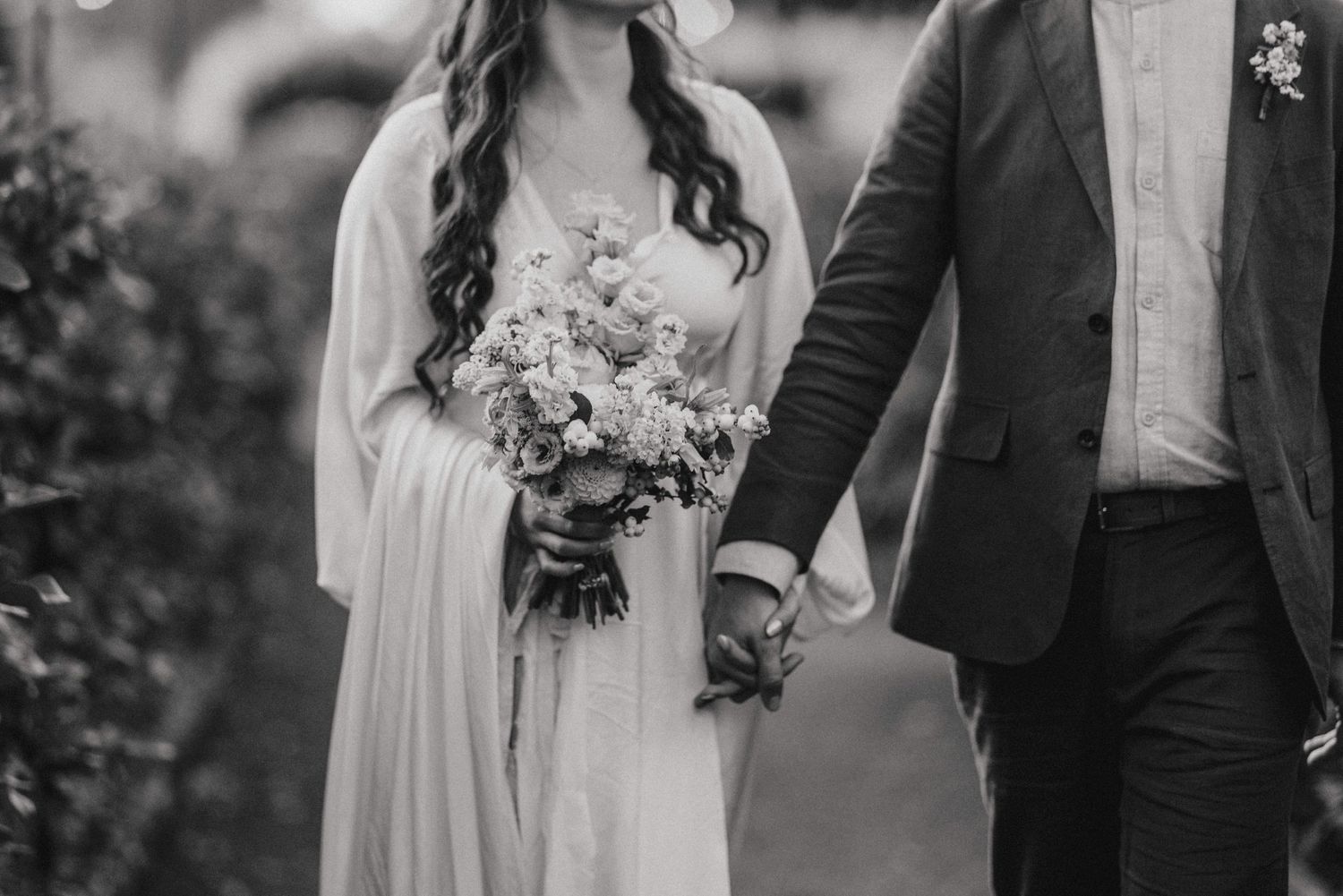 Wedding couple walking together with floral bouquet in elegant formal attire. Image taken by Lincolnshire photographers.