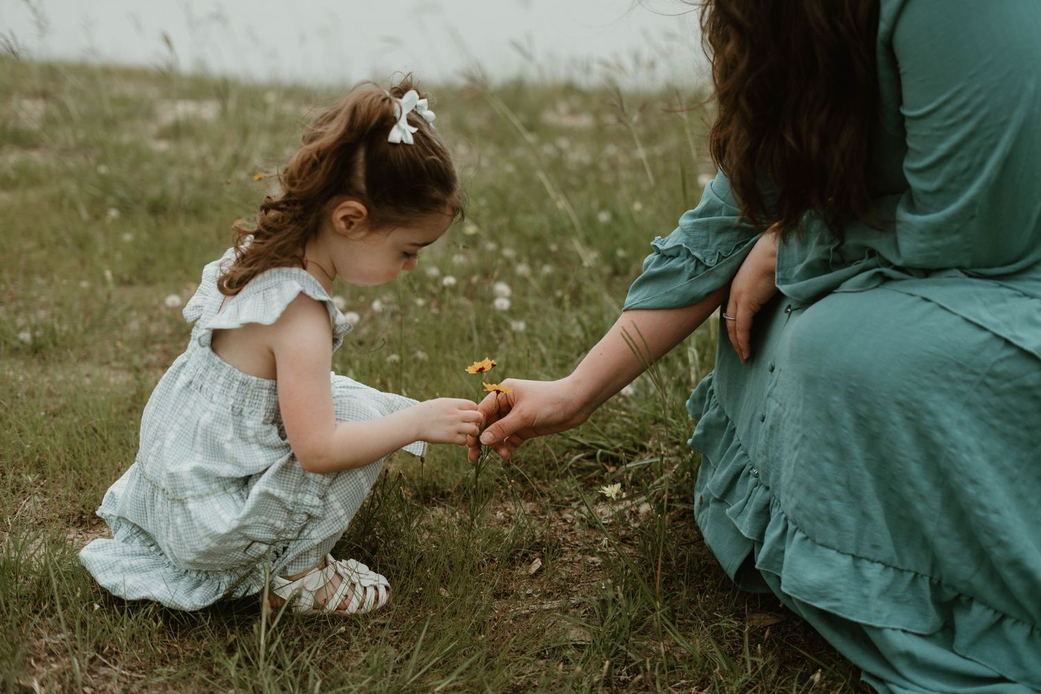 A sweet outdoor moment as a small child in white dress examines something in an adult's hand.