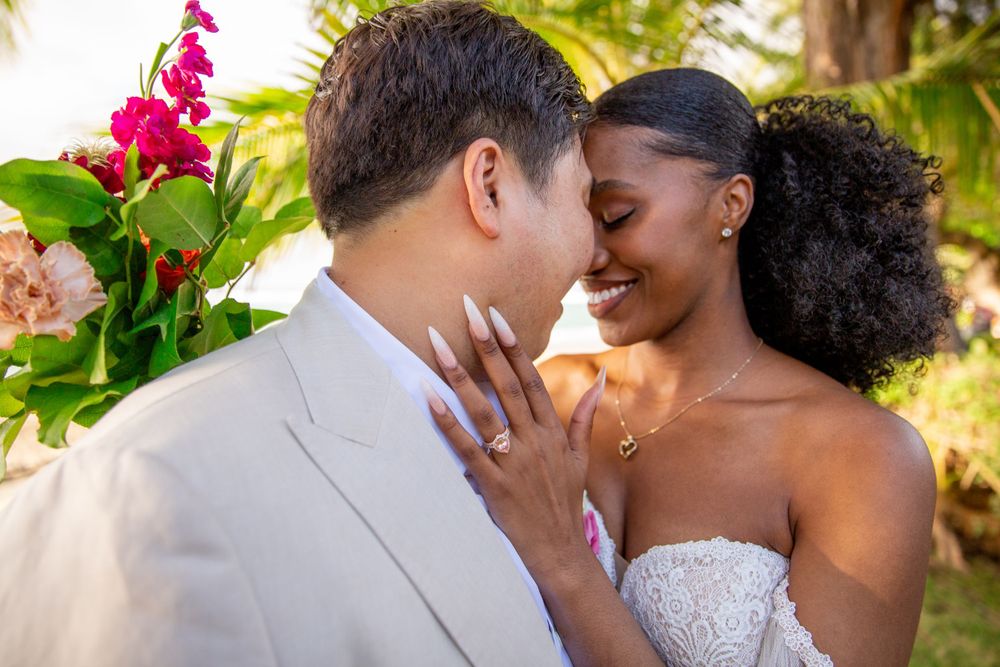 A tender wedding moment between newlyweds embracing outdoors with pink flowers and palm trees in the background of Haleiwa.
