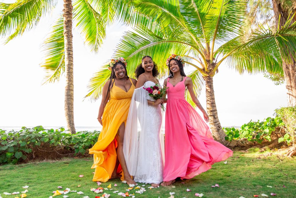 Bride and bridesmaids flair their pink and orange wedding dresses with palm trees in the background of Haleiwa.