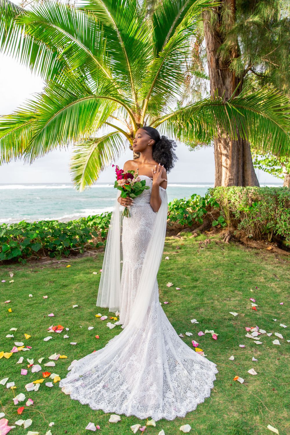 A stunning beach wedding scene with a white lace gown against palm trees and ocean backdrop in Haleiwa.