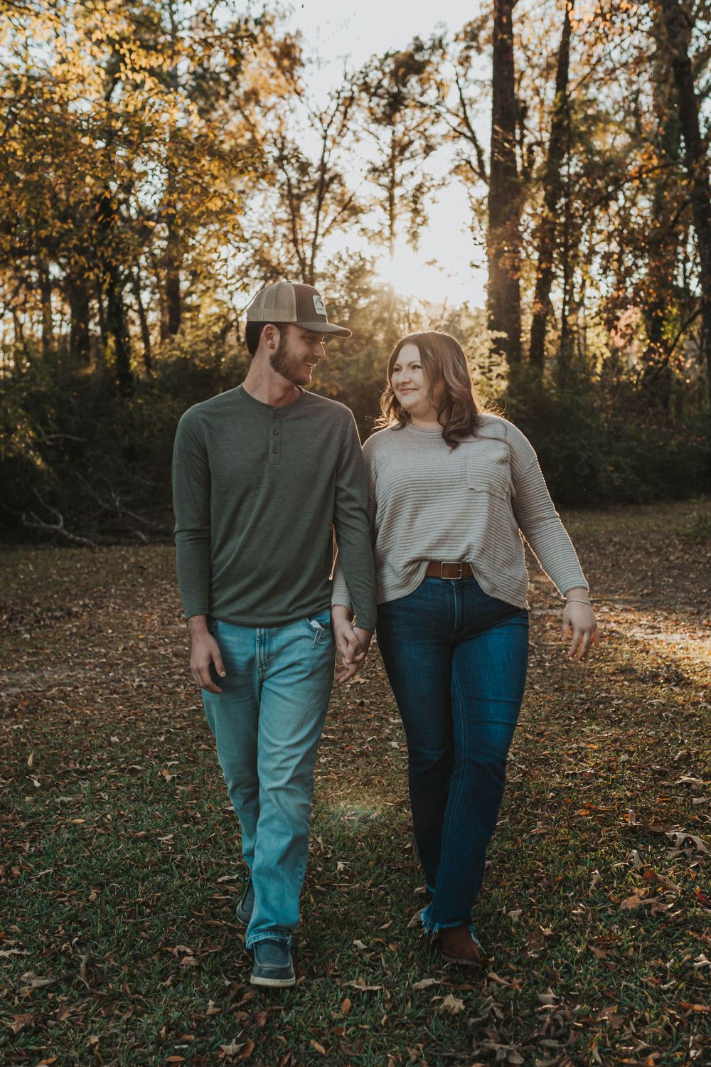 A couple walking together through a sunlit autumn forest wearing casual clothes.