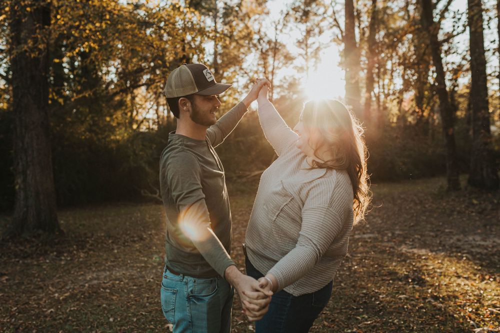 Couple sharing an intimate moment in a forest with sunlight streaming through trees.