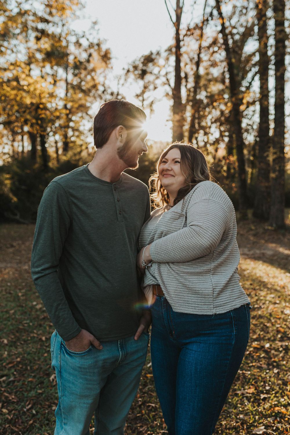A romantic couple embracing and laughing in a golden-lit wooded area during sunset.