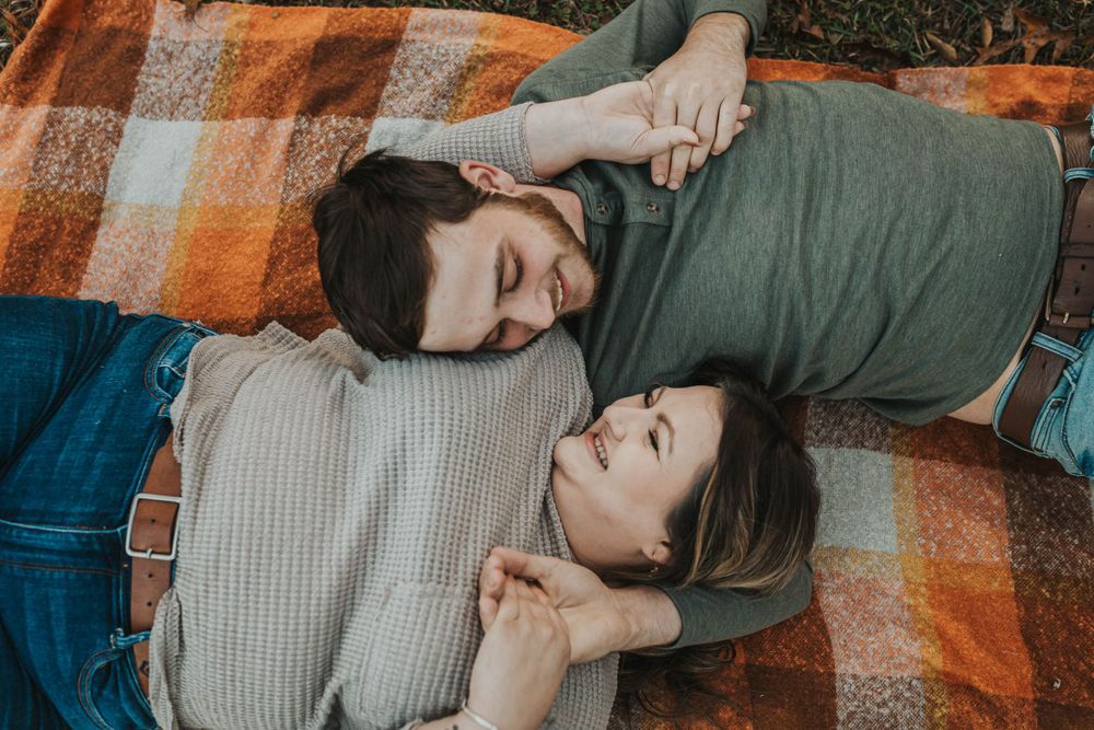 Couple cuddling on a plaid blanket during golden hour in nature.