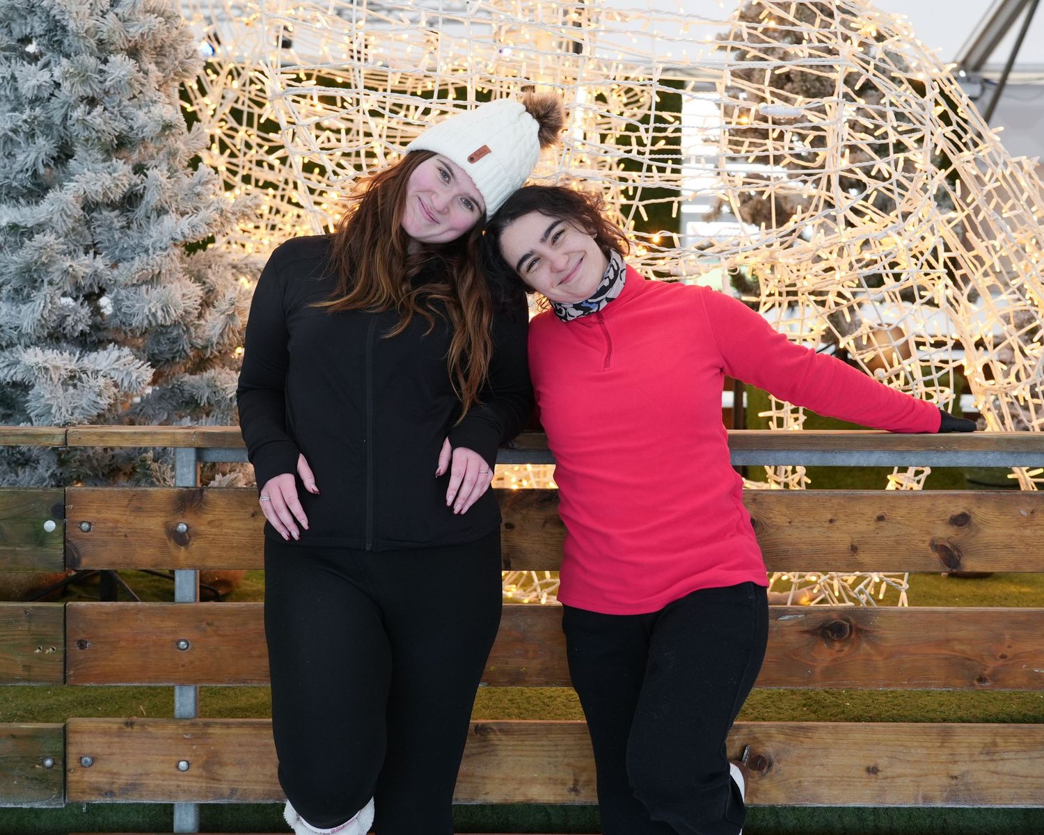 Two people in black and red outfits pose playfully against a rustic stone wall background.