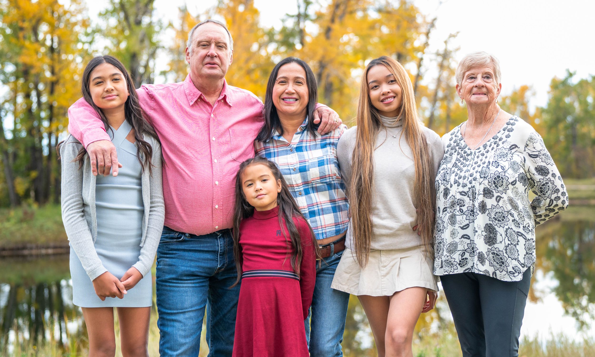 A family is smiling and posing for a photo in a park during fall.
