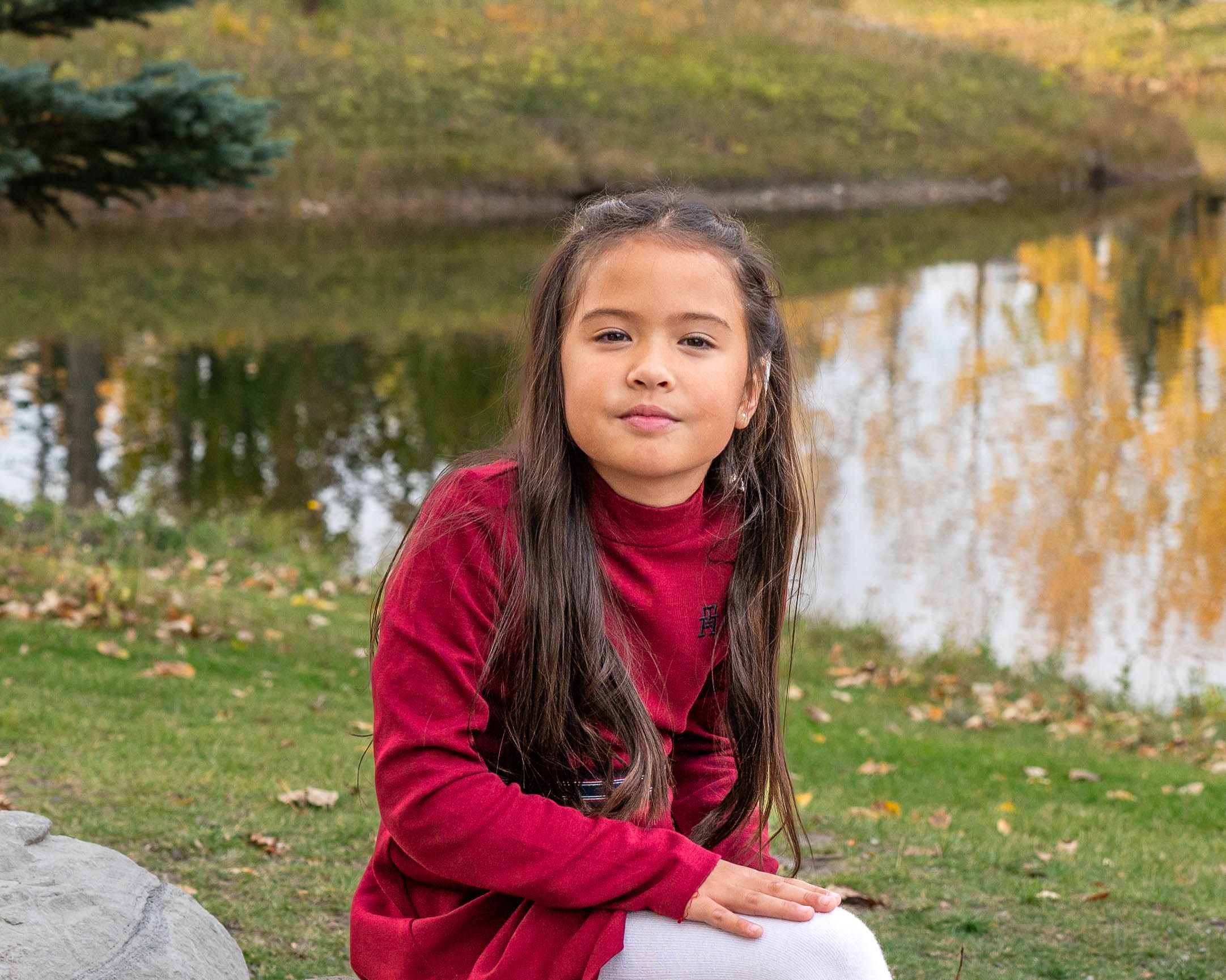 A little girl sitting in the park wearing a red dress during fall.