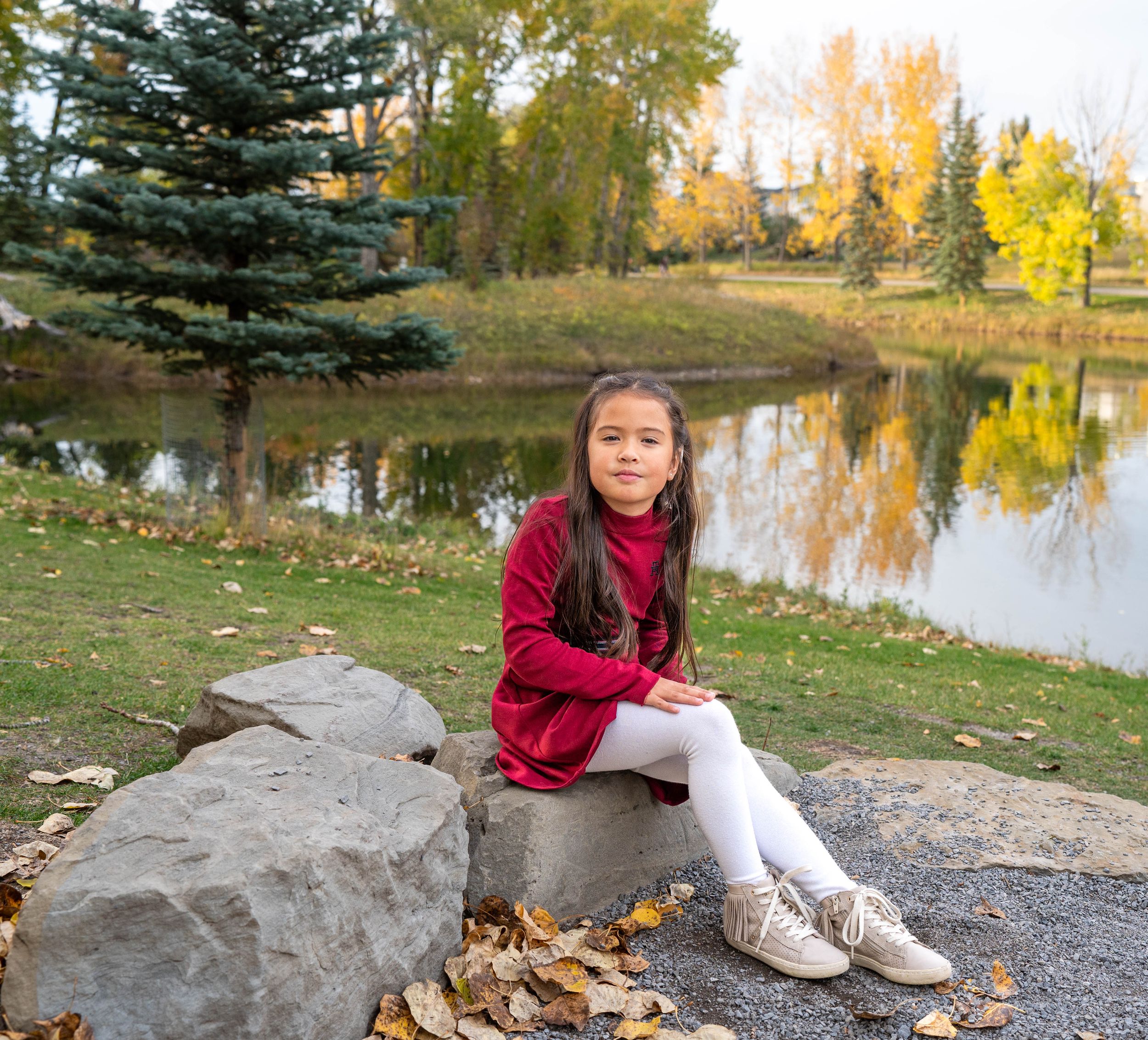 A little girl sitting in the park wearing a red dress during fall.