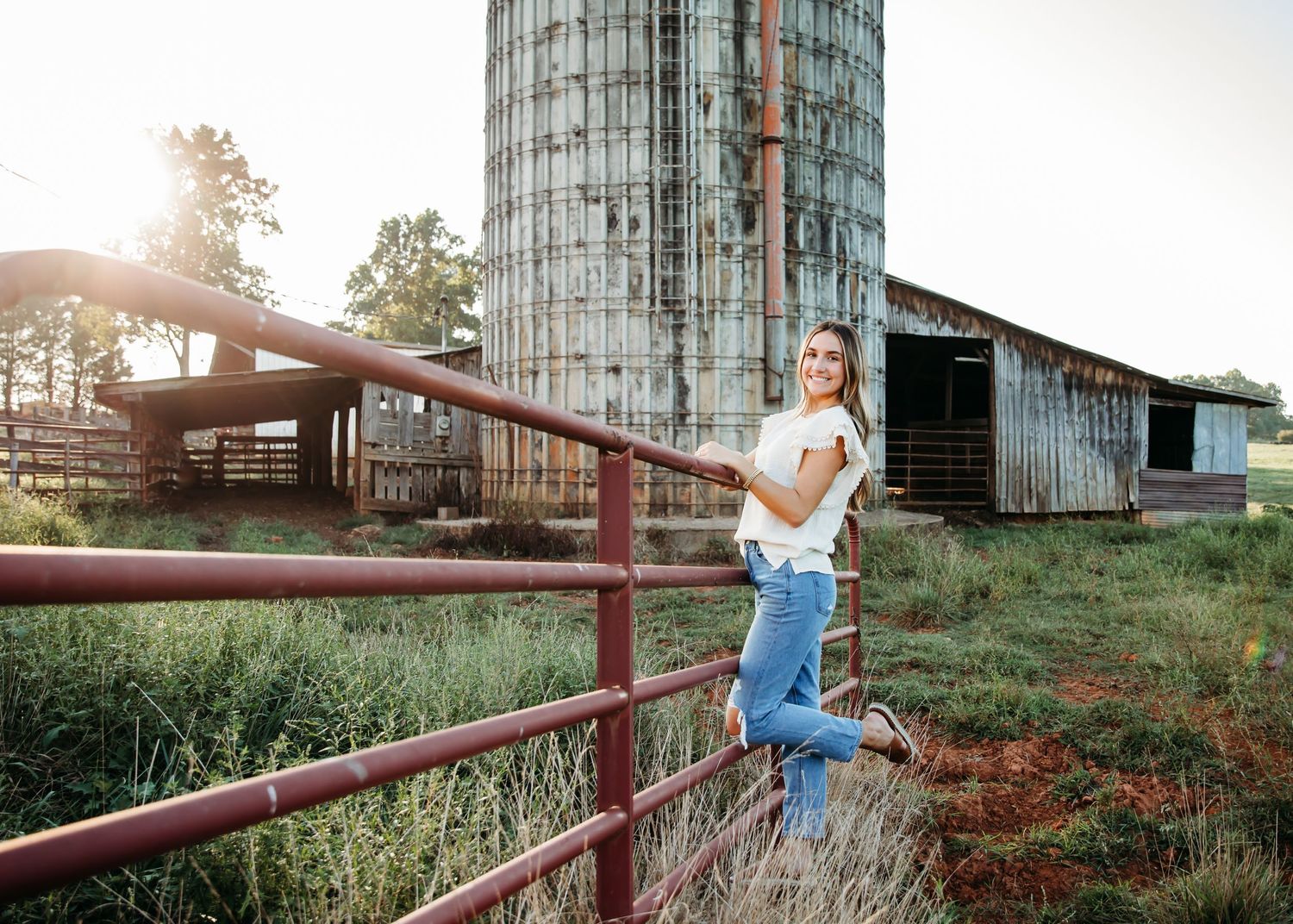 Rustic senior photos taken at sunset by a wooden fence and barn.