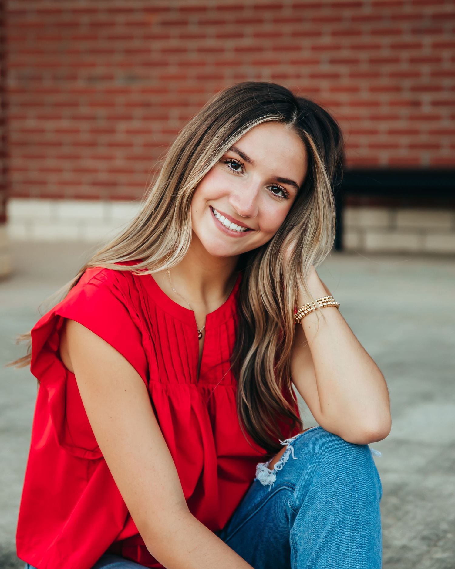 Senior portrait session featuring a red top and blue jeans against a brick wall background.