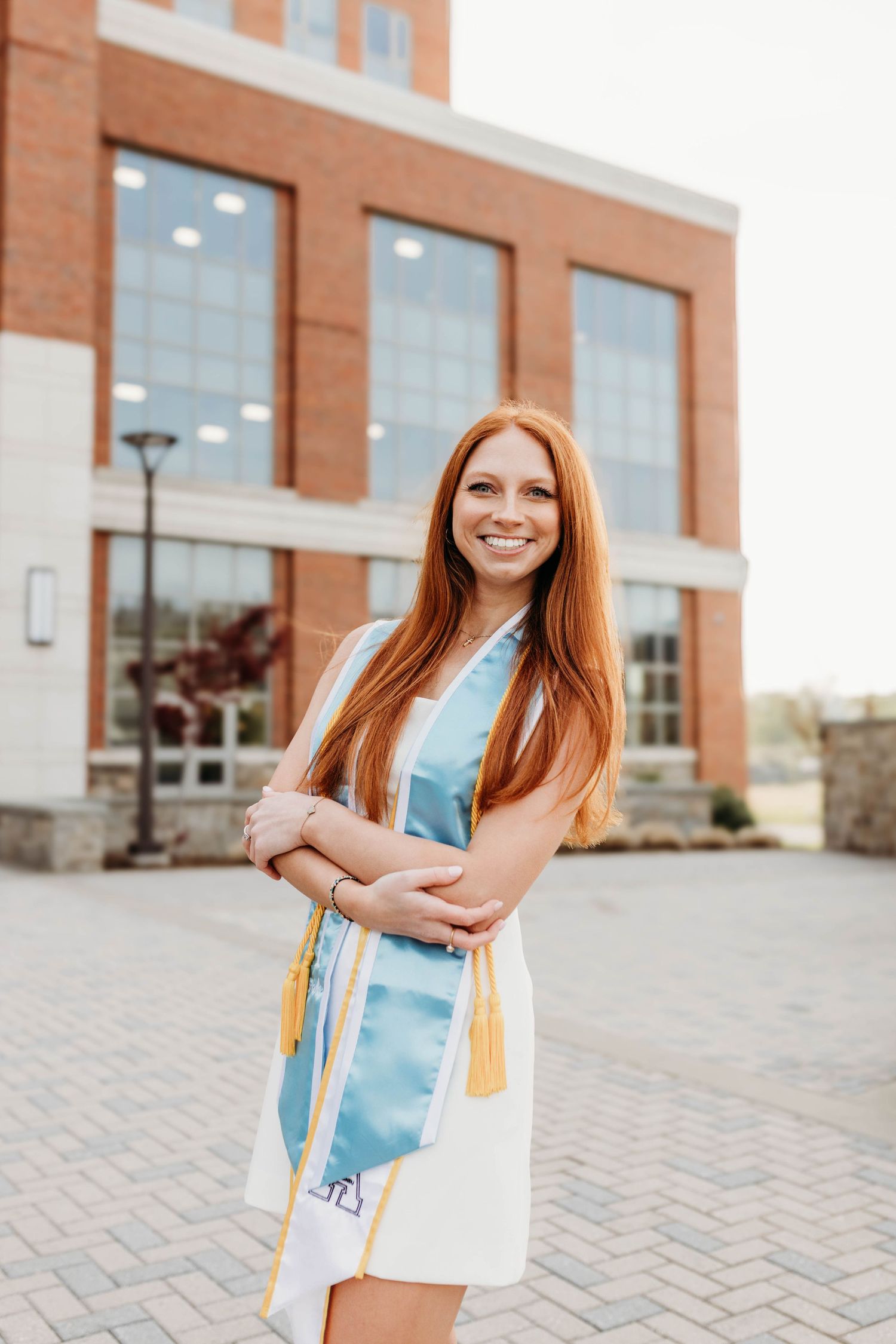 Student celebrates graduation with joyful poses outside modern brick university building.